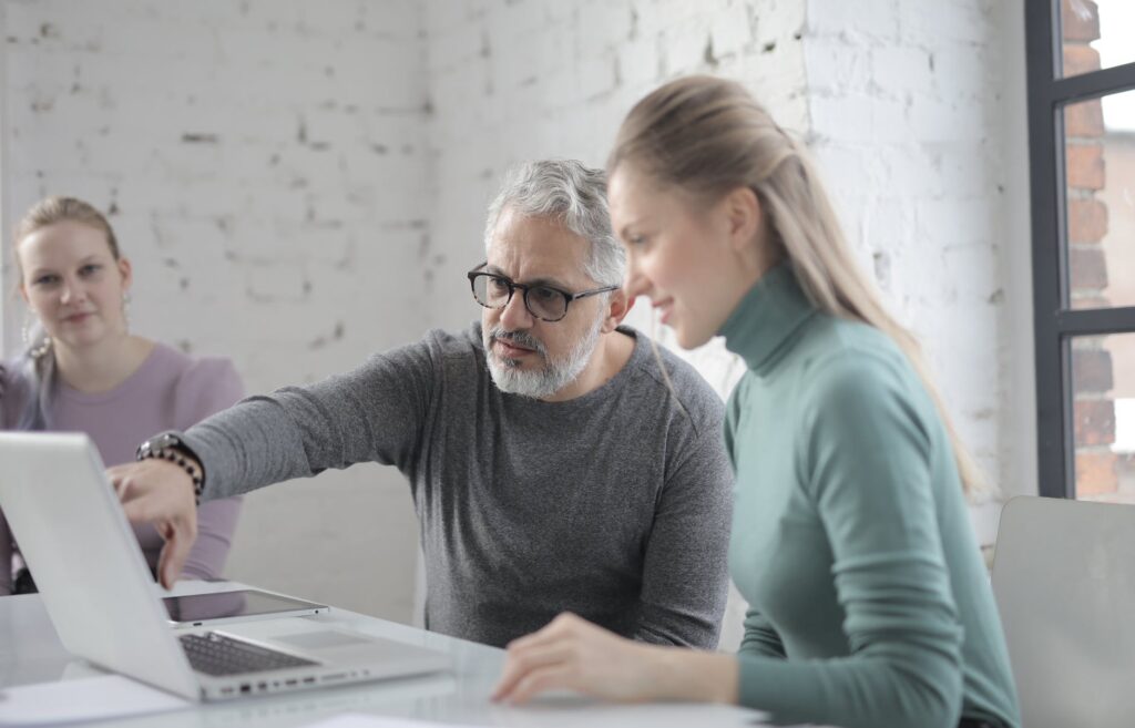 mature man using laptop while discussing information with colleague